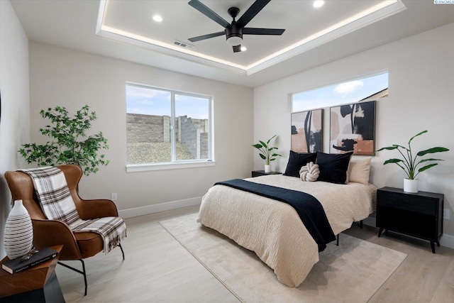 bedroom featuring ceiling fan, a tray ceiling, and light wood-type flooring