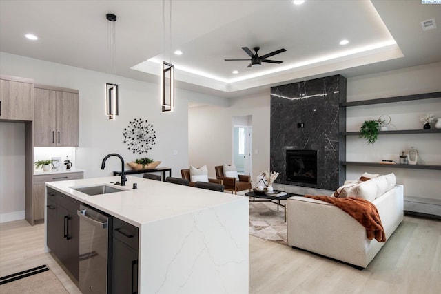 kitchen with a tray ceiling, decorative light fixtures, a kitchen island with sink, and sink