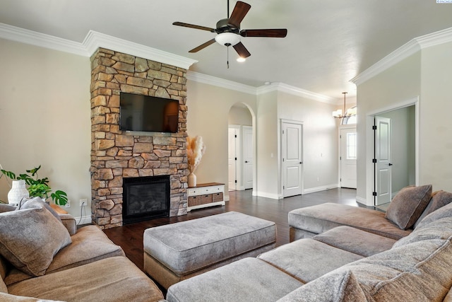 living room featuring ornamental molding, ceiling fan with notable chandelier, a stone fireplace, and arched walkways