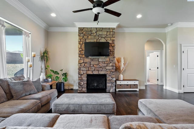 living room featuring dark wood-style floors, ceiling fan, a stone fireplace, ornamental molding, and arched walkways