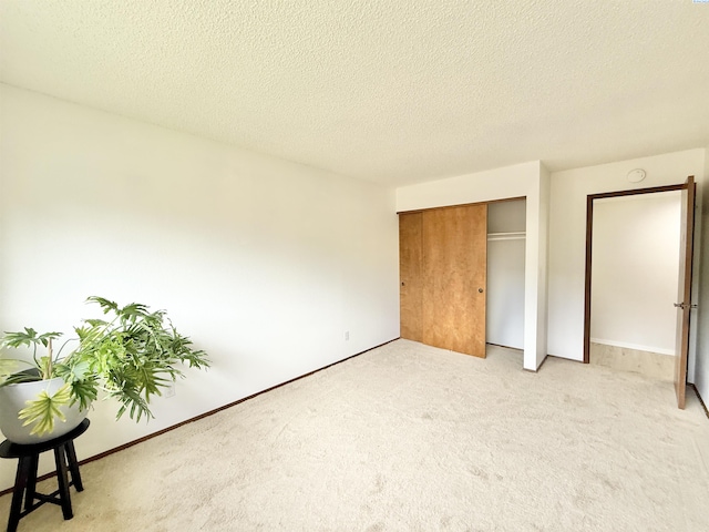 unfurnished bedroom featuring light colored carpet, a closet, a textured ceiling, and baseboards
