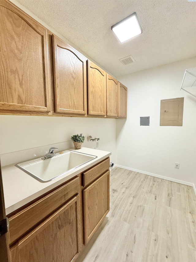 laundry area with hookup for a washing machine, light wood-style floors, cabinet space, electric panel, and a textured ceiling