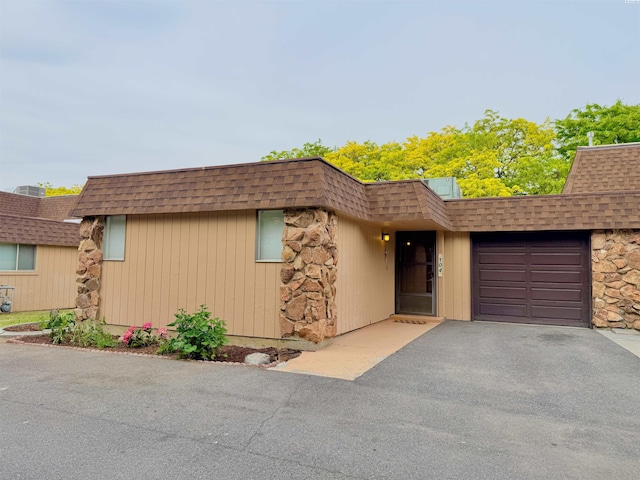 view of front of property featuring mansard roof, driveway, a shingled roof, and a garage