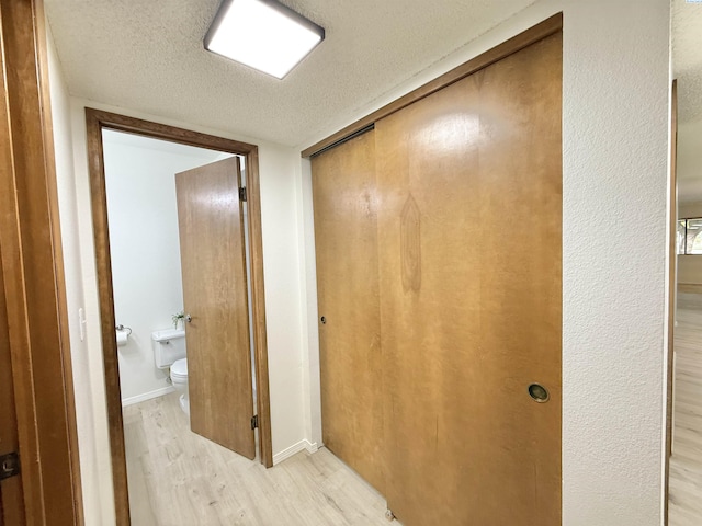 hall with light wood-style floors, a textured ceiling, and baseboards