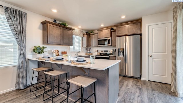 kitchen with appliances with stainless steel finishes, sink, a breakfast bar area, and light hardwood / wood-style flooring