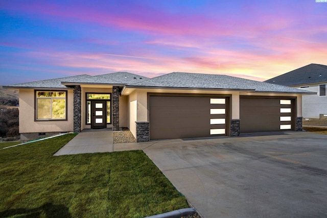 prairie-style house featuring an attached garage, concrete driveway, stone siding, stucco siding, and a front lawn