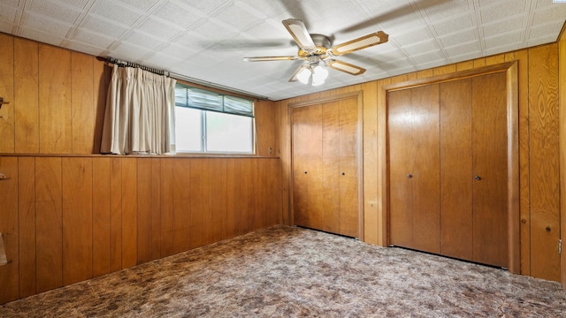 unfurnished bedroom featuring ceiling fan, wood walls, carpet flooring, and multiple closets
