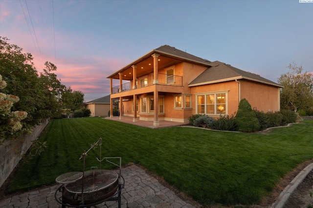 back house at dusk with a balcony, an outdoor fire pit, a yard, and a patio area