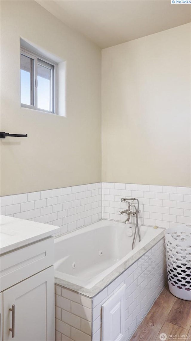 bathroom with hardwood / wood-style floors, vanity, tiled bath, and tile walls