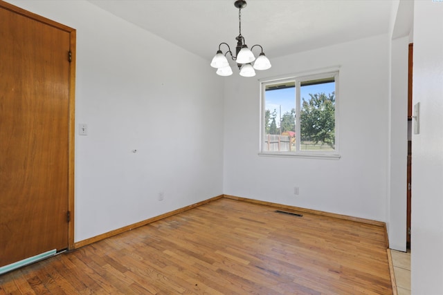 spare room featuring light hardwood / wood-style flooring and a notable chandelier