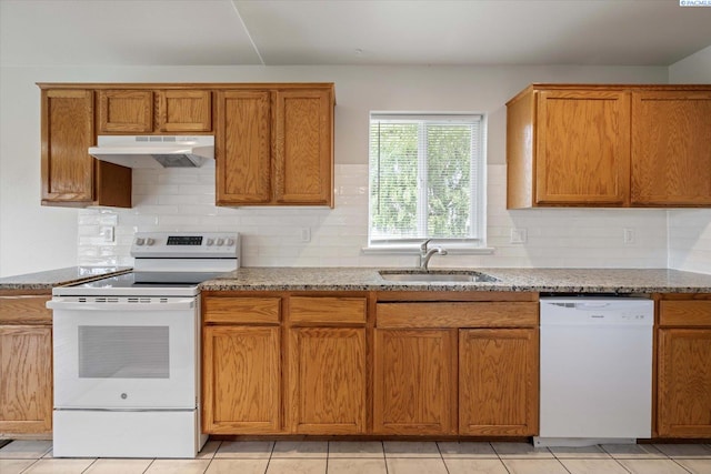 kitchen featuring light stone countertops, brown cabinets, a sink, under cabinet range hood, and white appliances