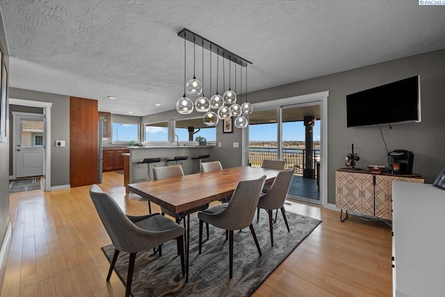 dining room featuring a textured ceiling, light wood finished floors, and baseboards