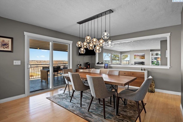 dining area with a textured ceiling, light wood finished floors, an inviting chandelier, and baseboards