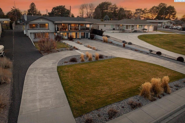 view of front of home with concrete driveway, a lawn, and a balcony