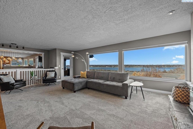 living room with carpet flooring, a water view, a textured ceiling, and baseboards