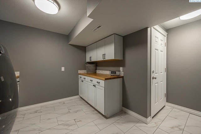 kitchen featuring marble finish floor, visible vents, baseboards, and wooden counters