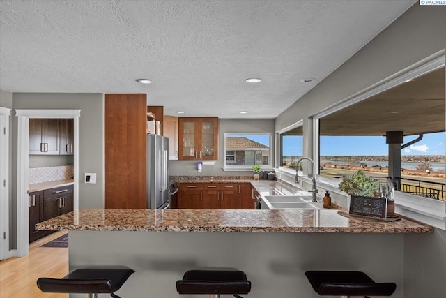 kitchen with a peninsula, a sink, freestanding refrigerator, light stone countertops, and glass insert cabinets