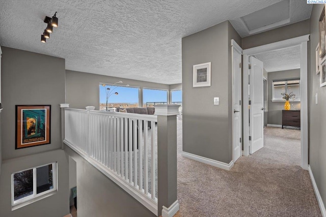 hallway featuring a textured ceiling, carpet flooring, an upstairs landing, and baseboards