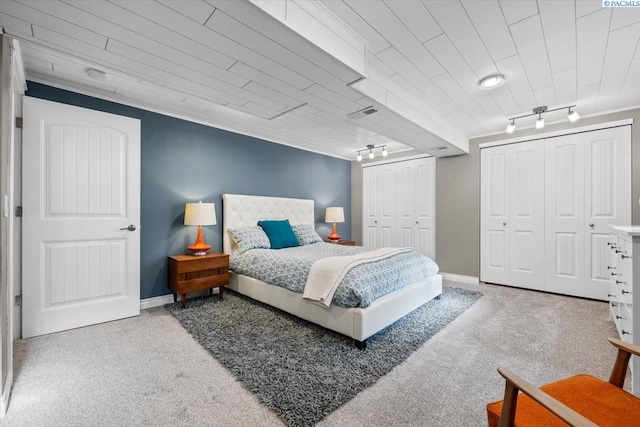 carpeted bedroom with rail lighting, visible vents, baseboards, and two closets