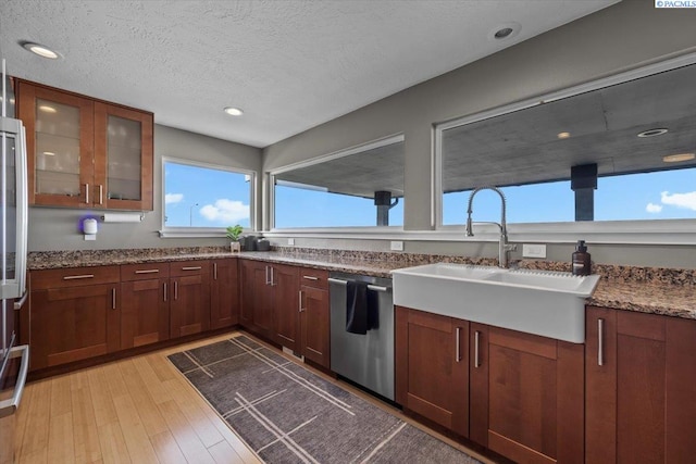 kitchen with dishwasher, glass insert cabinets, a textured ceiling, light wood-type flooring, and a sink