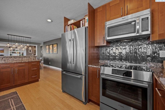 kitchen with tasteful backsplash, appliances with stainless steel finishes, brown cabinetry, and light wood-style flooring