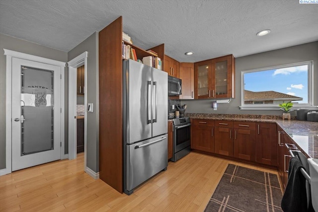 kitchen with a textured ceiling, stainless steel appliances, light wood-style flooring, and glass insert cabinets