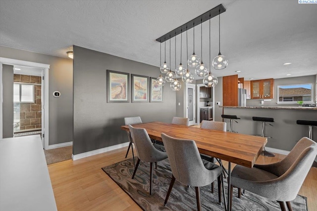 dining area featuring baseboards, a textured ceiling, and light wood-style floors