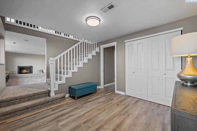 entrance foyer featuring visible vents, wood finished floors, a lit fireplace, baseboards, and stairs