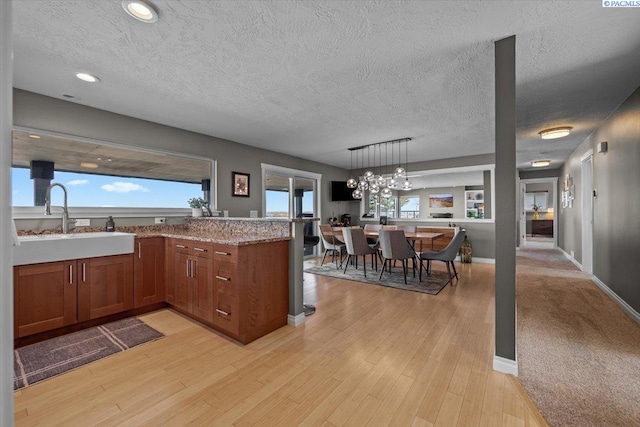 kitchen with hanging light fixtures, light wood finished floors, brown cabinetry, and light stone countertops