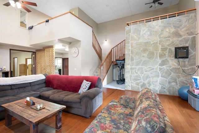 living room with a drop ceiling, a towering ceiling, ceiling fan, and light wood-type flooring