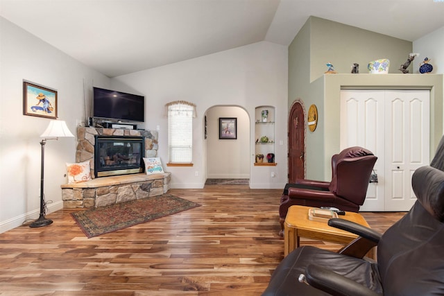 living room with lofted ceiling, a stone fireplace, and wood-type flooring