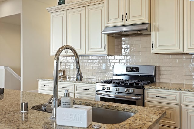 kitchen with light stone counters, decorative backsplash, stainless steel gas range oven, and cream cabinetry