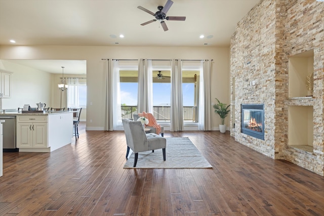 unfurnished living room featuring dark hardwood / wood-style floors, ceiling fan with notable chandelier, and a stone fireplace