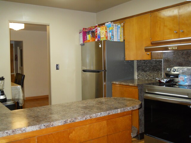 619 Grandview Ave, Sunnyside, WA 98944 - kitchen featuring brown cabinets, under cabinet range hood, wood finished floors, decorative backsplash, and appliances with stainless steel finishes