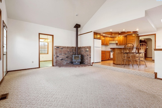 unfurnished living room with visible vents, light colored carpet, a wood stove, heating unit, and high vaulted ceiling