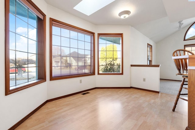 unfurnished room with lofted ceiling with skylight, visible vents, light wood-style floors, and baseboards