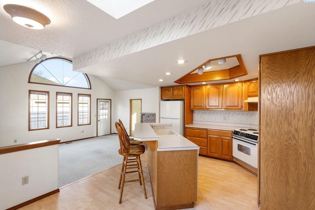 kitchen with white appliances, lofted ceiling, a breakfast bar, light countertops, and under cabinet range hood