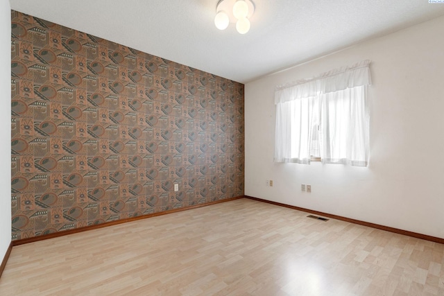 spare room featuring visible vents, a textured ceiling, baseboards, and wood finished floors