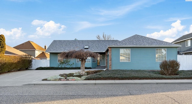 ranch-style home featuring concrete driveway, a shingled roof, and fence