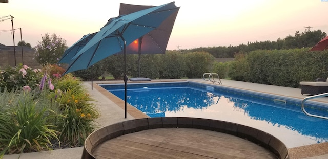 pool at dusk featuring an outdoor pool and a patio