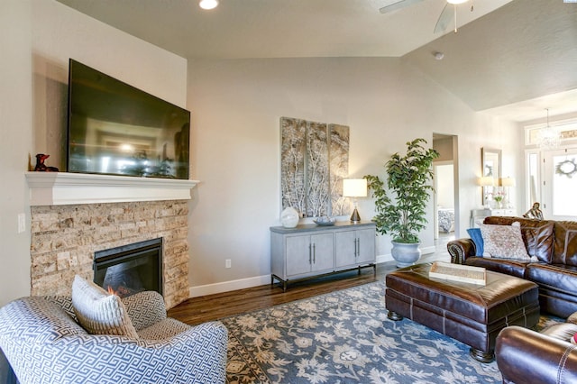 living room with lofted ceiling, ceiling fan, a stone fireplace, wood finished floors, and baseboards