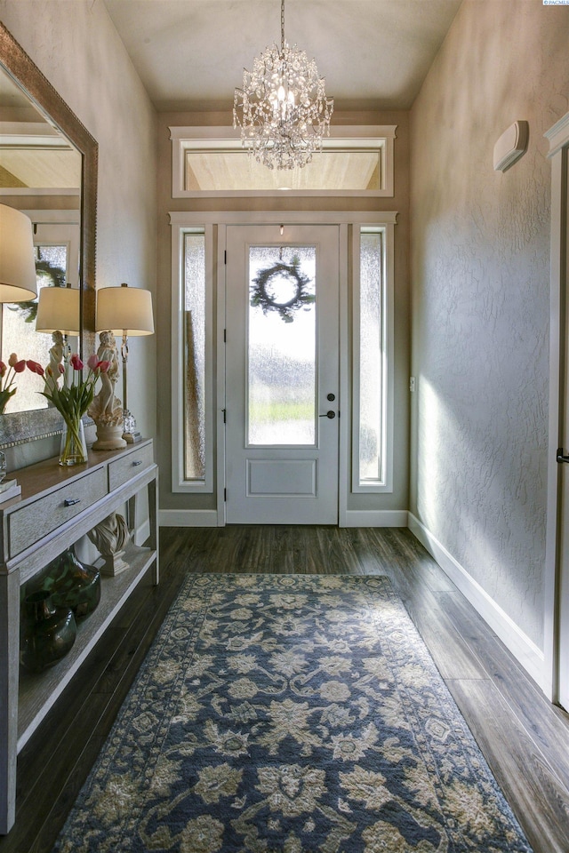 entryway featuring a notable chandelier, a textured wall, wood finished floors, and baseboards