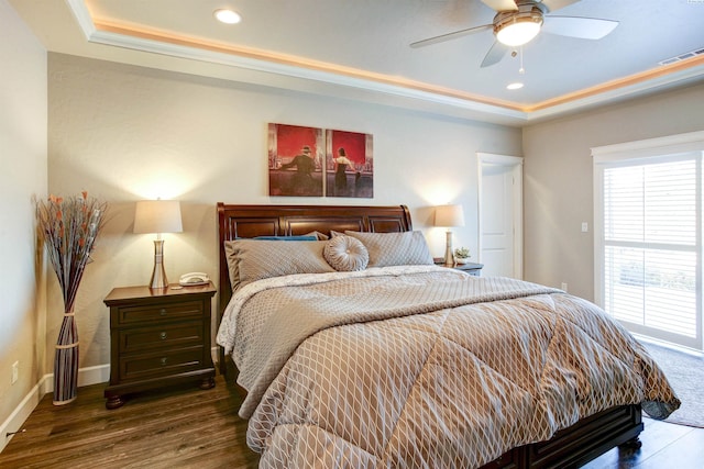 bedroom featuring a tray ceiling, wood finished floors, visible vents, and baseboards