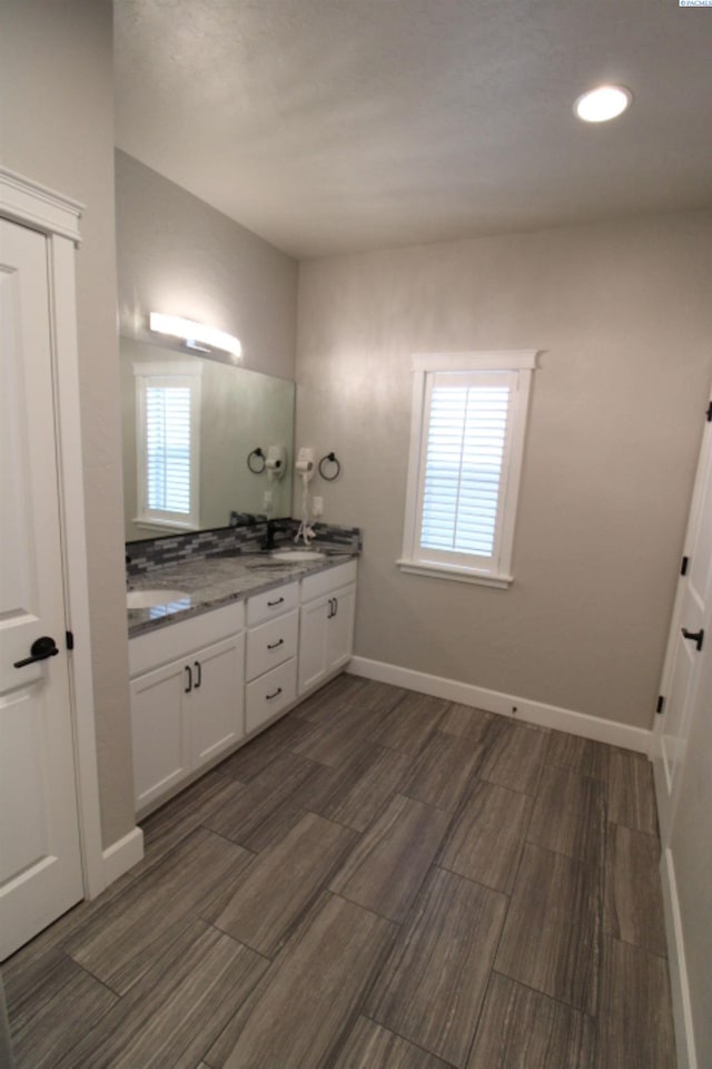 bathroom with wood finish floors, a sink, baseboards, and double vanity