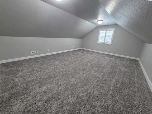 bonus room with a textured ceiling, visible vents, baseboards, vaulted ceiling, and dark colored carpet