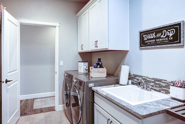 washroom with baseboards, cabinet space, a sink, and washing machine and clothes dryer