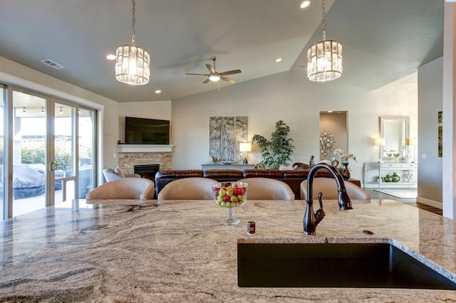 kitchen with open floor plan, a sink, a stone fireplace, and light stone countertops