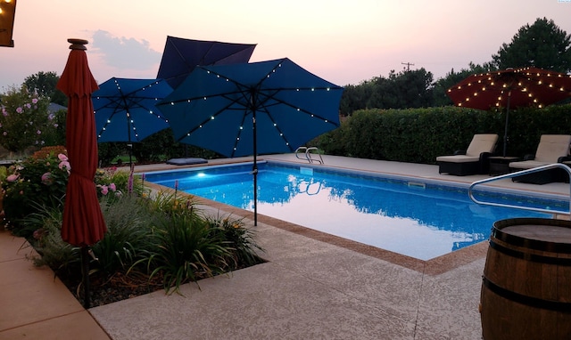 pool at dusk with a patio area and an outdoor pool