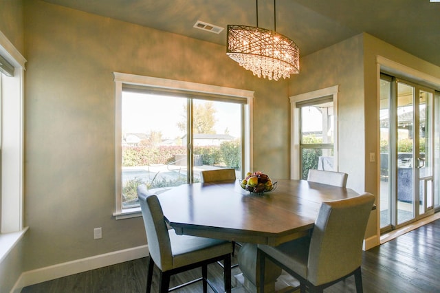 dining area with dark wood-type flooring, an inviting chandelier, visible vents, and baseboards