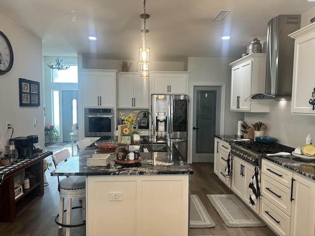 kitchen featuring wall chimney exhaust hood, stainless steel appliances, and a center island with sink